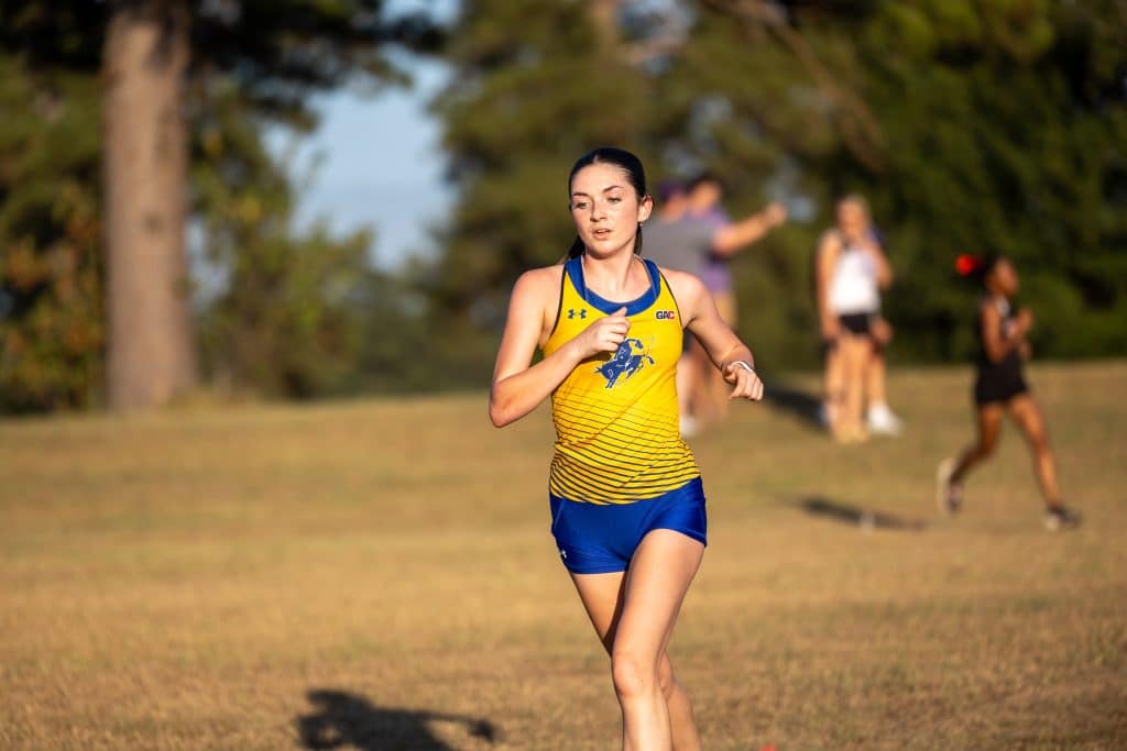 A Mulerider runner in a gold and blue uniform races across a grass course at sunset