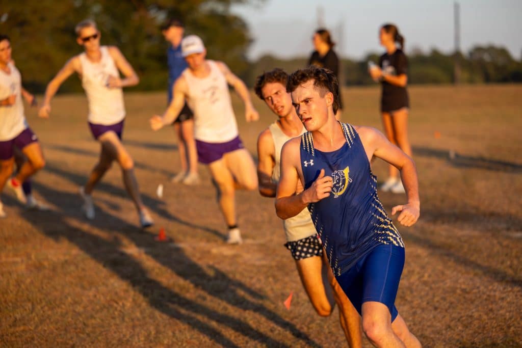 A Mulerider distance runner leads a pack of competitors across an open field