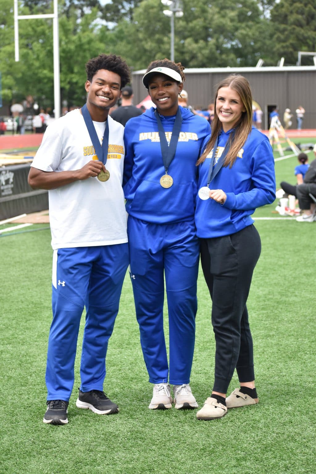 A Mulerider athlete wearing a medal stands on the infield with two SAU supporters
