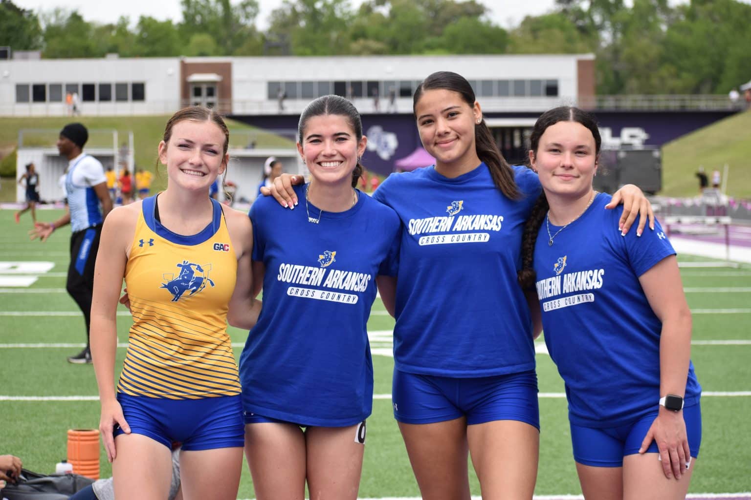 Four smiling Mulerider Track and Field athletes pose together at a meet